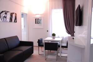 A modern living room with a black sofa, a dining table with two chairs, a small potted plant, and artwork on the walls. - Rapallo Suites (Rapallo)