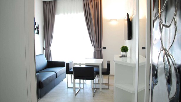 Ein modernes Wohnzimmer mit einer Couch, einem Esstisch und Stühlen. Ein Fernseher ist an der Wand montiert und auf dem Seitentisch steht eine kleine Pflanze.