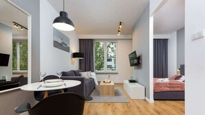 Ett modernt och väl upplyst vardagsrum med en soffa, ett matbord med stolar, ett soffbord och en säng med ett rosa överkast.