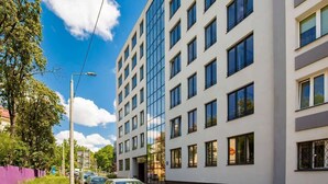 En modern byggnad med flera våningar, stora fönster och en parkeringsplats med bilar.