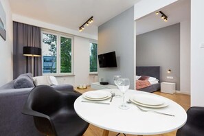 Un salon moderne comprenant un coin repas, un canapé gris, un téléviseur à écran plat et de grandes fenêtres.