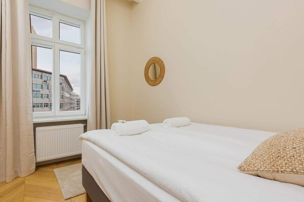 A bedroom with a bed, a window with curtains, a radiator, and a wall-mounted mirror.