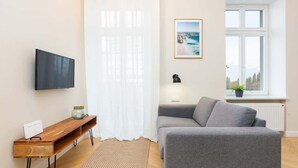 Una sala moderna con un sofá gris, una mesita de madera, un televisor de pantalla plana, un cuadro enmarco y una ventana con vistas.