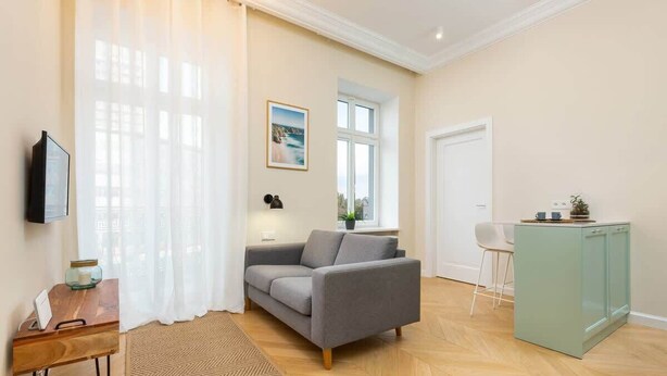 Una sala de estar moderna con un sofá gris, una mesita de madera, un armario verde y un ventanal con vistas.