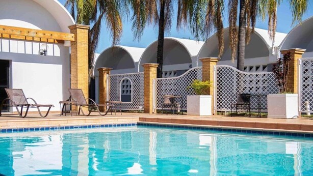 A swimming pool with lounge chairs and a covered area with arched ceilings. - Ibis Styles Rio Preto Monte Libano (São José do Rio Preto)