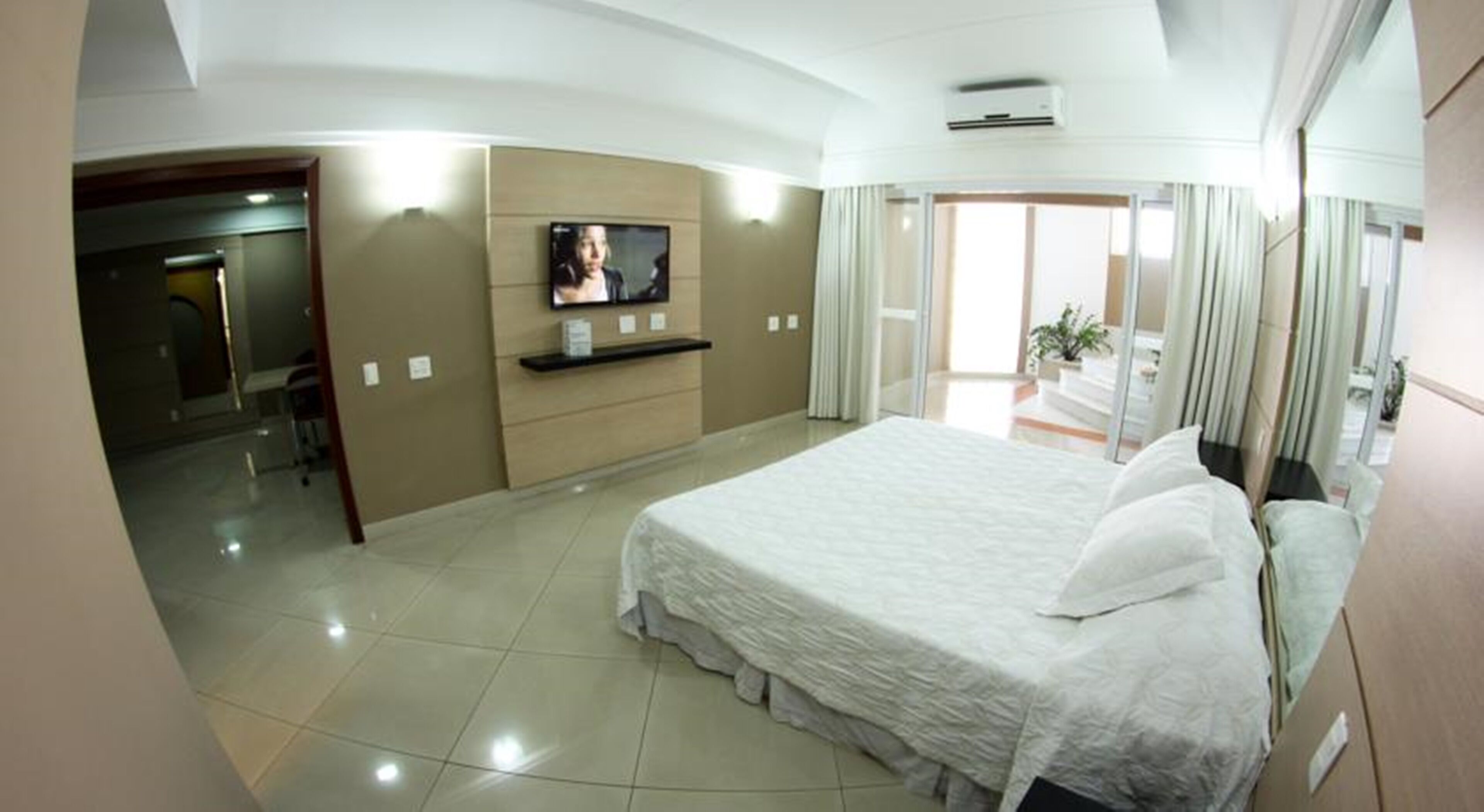 Habitación de hotel con una cama grande, un televisor en la pared y un ventanal corredero que da a un balcón.