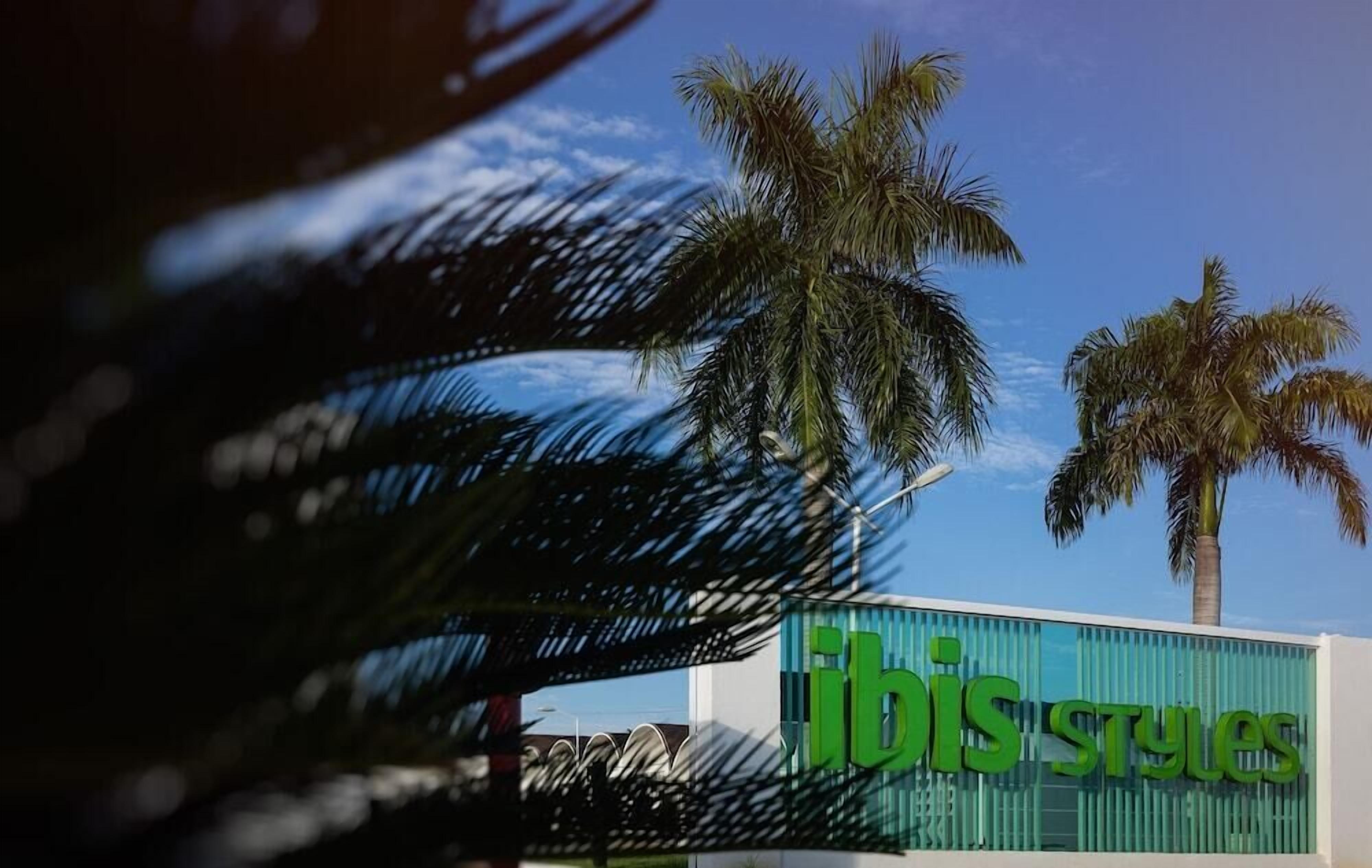 A building with a sign reading "ibis styles" and palm trees in the background.