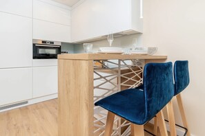 A modern kitchen with white cabinets, a built-in oven, and a wooden table with two blue chairs.