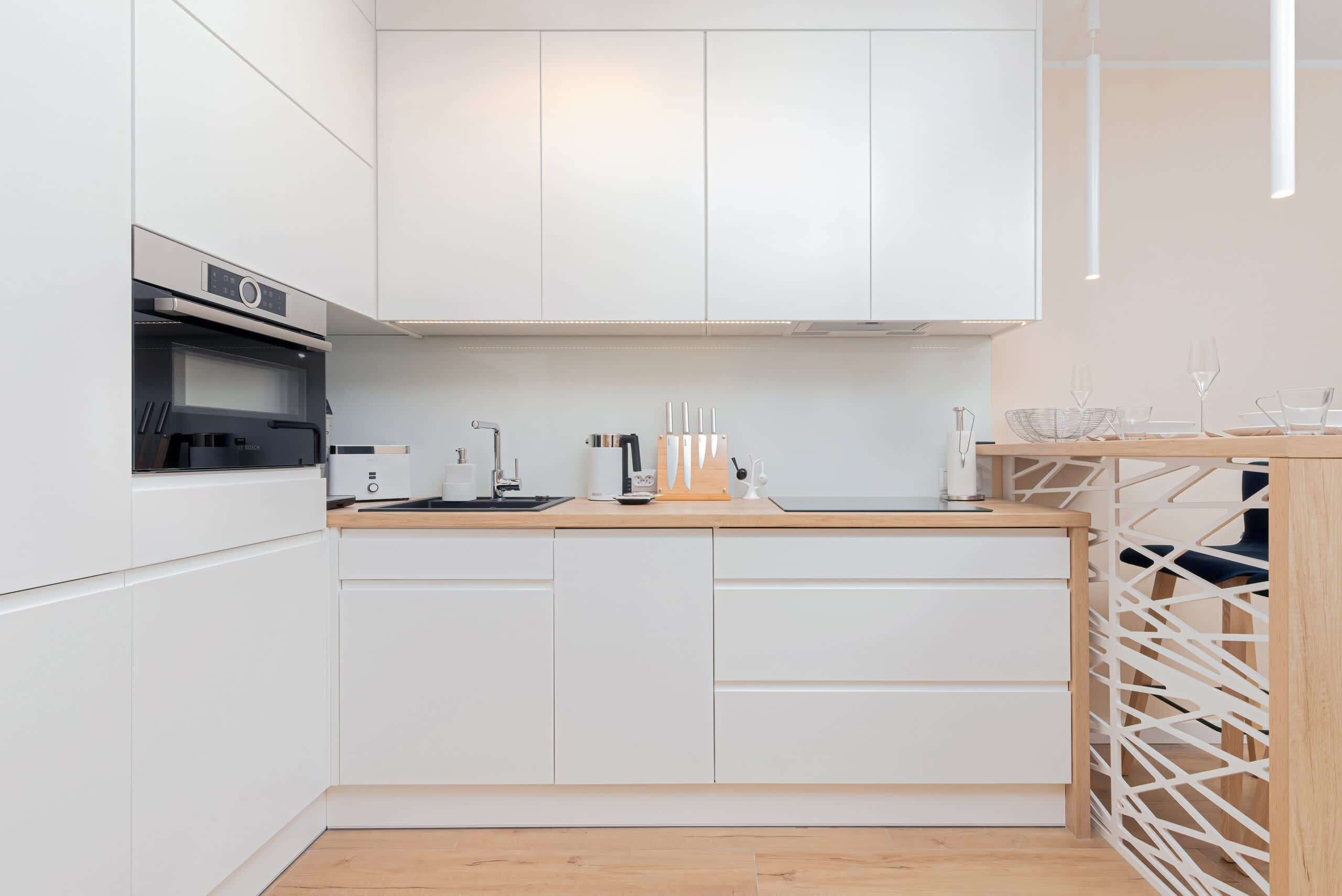 A modern kitchen with white cabinetry, a built-in oven, and a wooden countertop.