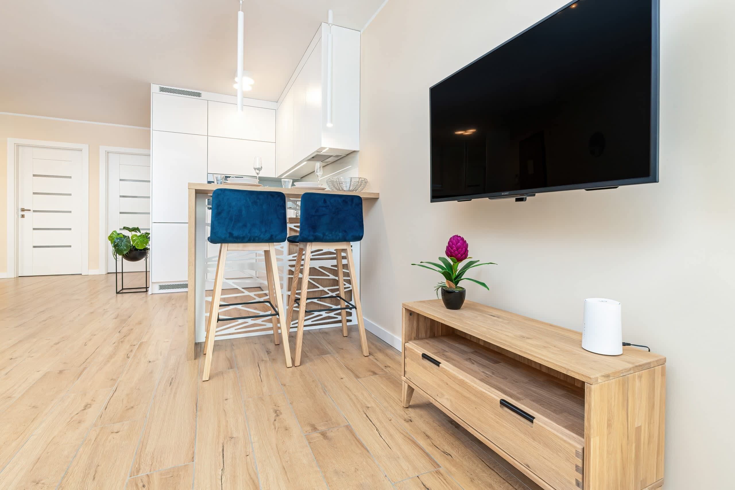 A modern living room with a wooden floor, a TV mounted on the wall, and a wooden console table with a plant.