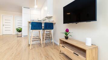 A modern living room with a wooden floor, a TV mounted on the wall, and a wooden console table with a plant.