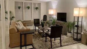 Una sala de estar moderna con un sofá, sillones, una mesa de centro, un televisor y lámparas de pie.