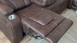 A reclining leather sofa with a massage function, a small table with a remote control, and a wall-mounted TV.