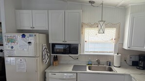 Una cocina compacta con armarios blancos, microondas, lavaplatos y un lavabo. Hay papeles y un calendario en el refrigerador.