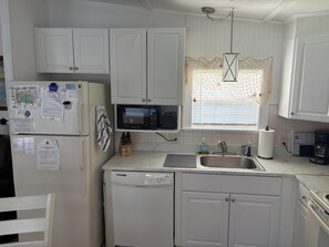 A compact kitchen with white cabinets, a microwave, a sink, and a dishwasher. There are papers and a calendar on the refrigerator. - Little cottage near the sea!  Golf CART is included! (Garden City)