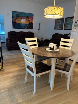 A dining area with a round table, white chairs, and a painting of a sunset on the wall. - SALE for November 2026! Little cottage near the sea!  Golf CART is included! (Garden City)