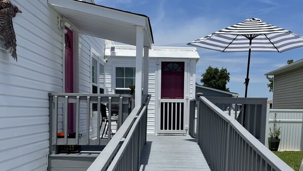 A wooden deck leading to a building with a covered porch and a striped umbrella.