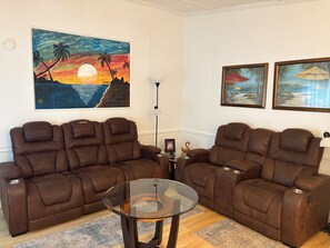 A living room with two brown leather sofas, a glass coffee table, and two framed beach paintings on the wall. - SALE for November 2026! Little cottage near the sea!  Golf CART is included! (Garden City)