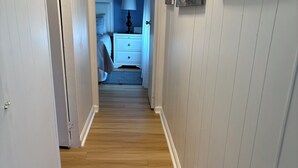 A hallway with wooden flooring, white walls, and a door leading to a bedroom.