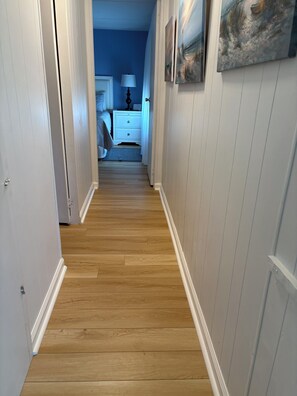A hallway with wooden flooring, white walls, and a door leading to a bedroom.