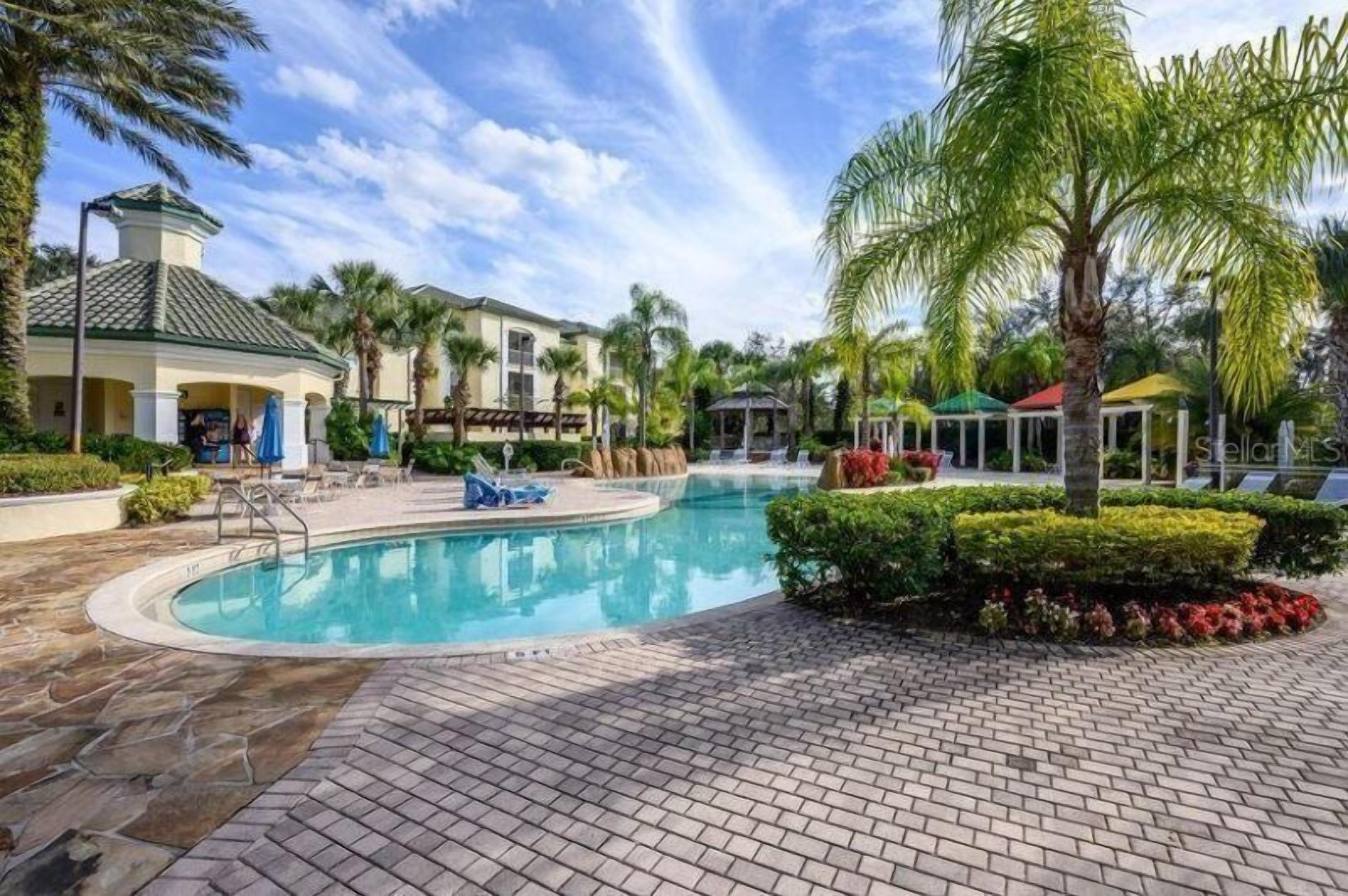 A pool area with a circular pool, lounge chairs, palm trees, and a building with a green roof.