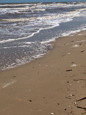 A beach with waves, scattered debris, and a clear sky. - Getaway By The Bay Unit 1 (Sargent)