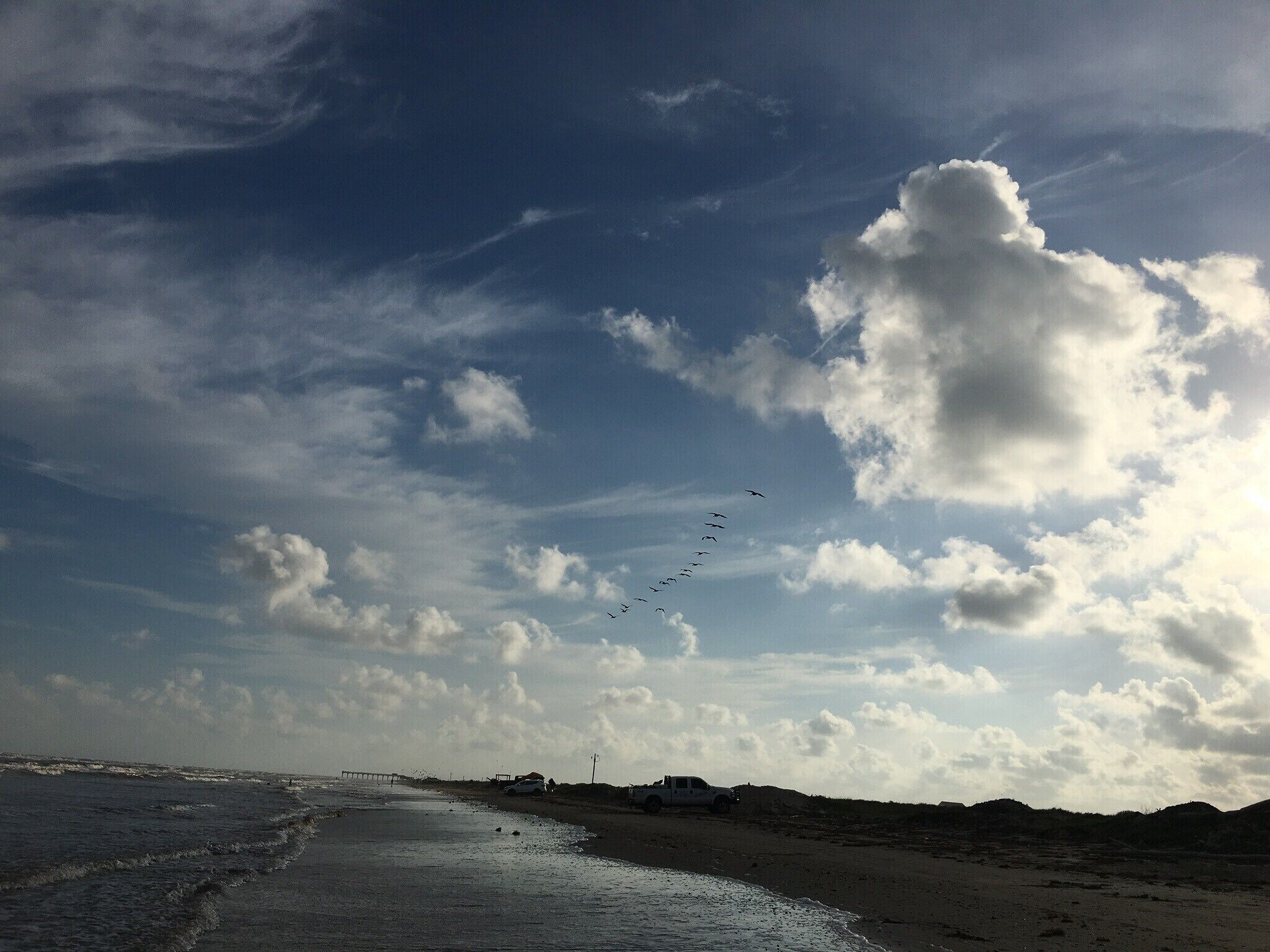 Ein Strand mit blauem Himmel, Wellen und einem entfernten Steg.