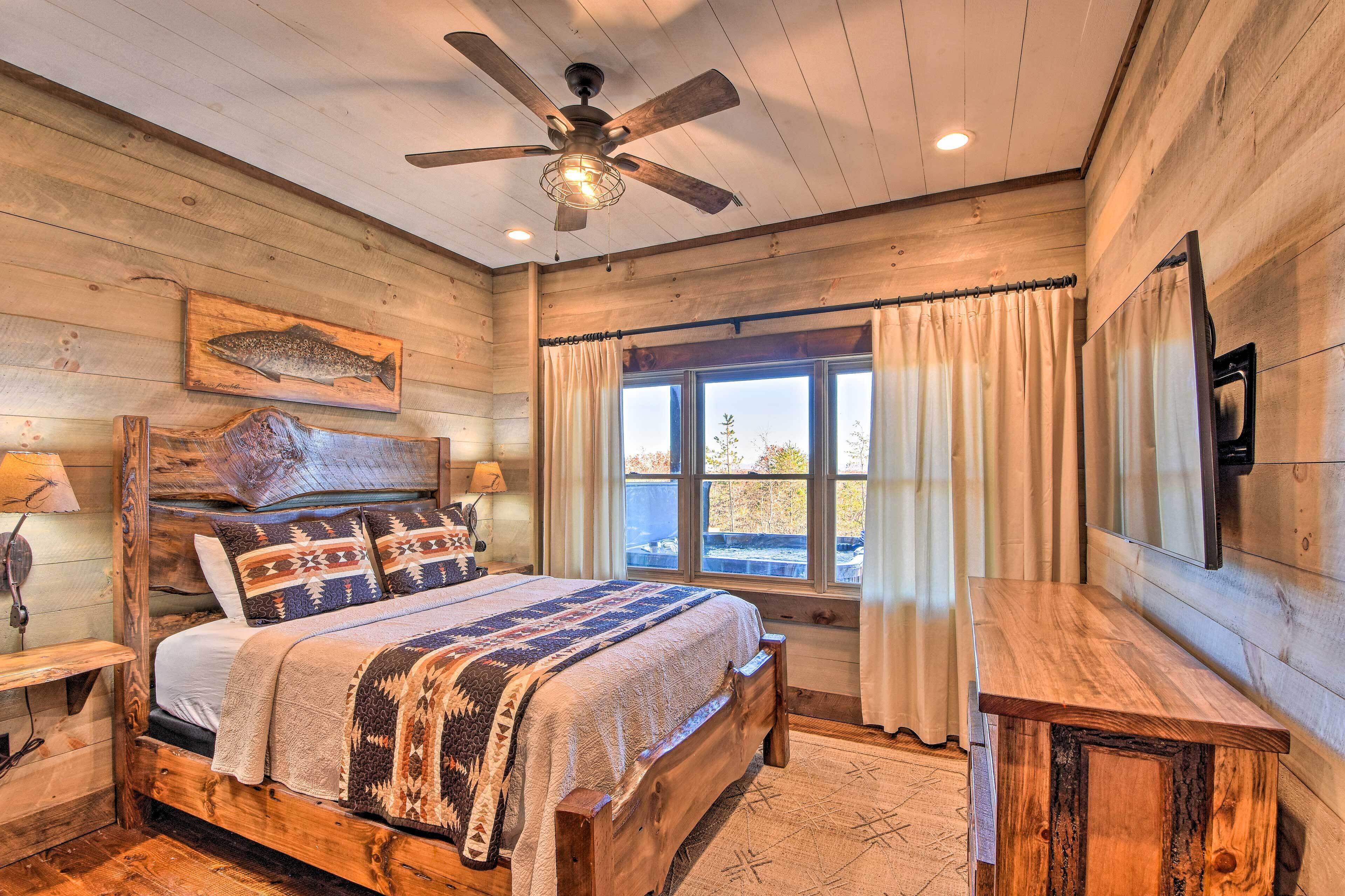 A wooden cabin bedroom with a bed, a ceiling fan, a window with curtains, and a wooden nightstand.