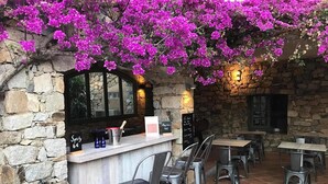 An outdoor cafe with stone walls, a bar area, and purple bougainvillea flowers. - Hotel Casa Rossa (L'Île-Rousse)