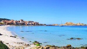A coastal town with clear blue waters, a sandy beach, and buildings along the shore. - Hotel Casa Rossa (L'Île-Rousse)