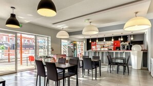 Un comedor moderno con mesas, sillas, una barra y lámparas colgantes.