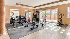 Un gimnasio amplio con diversos equipos de ejercicio, ventanas grandes y un techo alto.