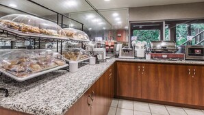 Un área de desayuno autoservicio con mostradores cubiertos para alimentos, una estación de café y vistas al exterior.