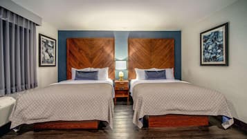 A hotel room with two beds, a wooden headboard, a nightstand with a lamp, and artwork on the walls.