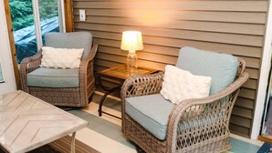 A cozy outdoor seating area with wicker chairs and a table, a lamp, and a view of the outdoors.