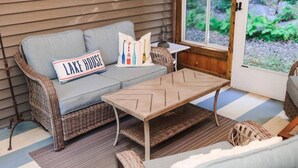 A wicker sofa with a cushion, a wooden coffee table, and a pillow with the text "LAKE HOUSE".
