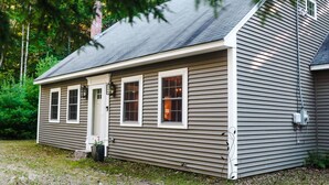 A single-story house with a grey siding exterior, a front door, and three windows.