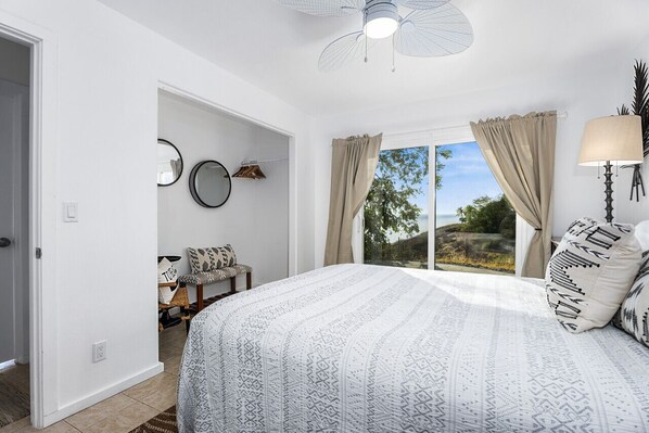 Un dormitorio con una cama grande, un ventilador de techo, vistas al exterior y una silla con cojines.