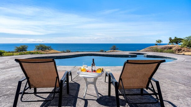 A poolside setting with two chairs and a table, overlooking a clear blue ocean.