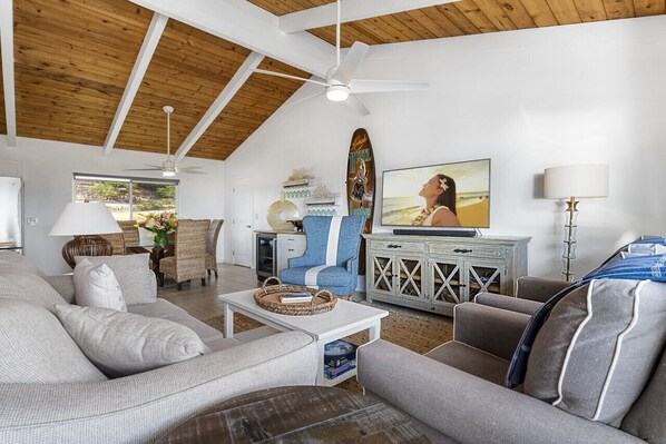 A spacious living room with a high ceiling, a television, and a beach-themed surfboard decoration.