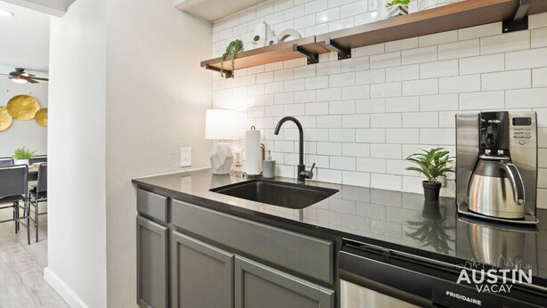 Een moderne keuken met een zwart spoelgedeelte, roestvrijstalen apparatuur en een houten plank met decoratieve objecten.