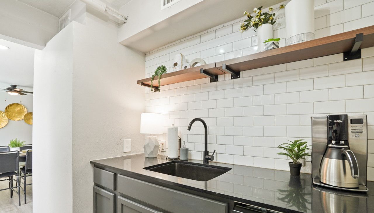 A modern kitchen with a black sink, stainless steel appliances, and a wooden shelf with decorative items.