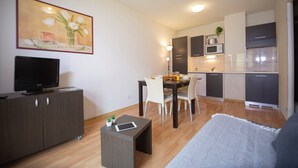 Een moderne woonkamer met een flatscreen-tv, een eethoek met een tafel en stoelen, en een keuken met donkere kasten en moderne apparatuur.