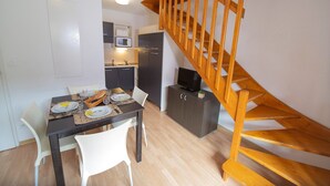 A compact living space with a dining area, kitchenette, and a wooden staircase. - Appartement Duplex Au Pied des Pistes (Les Orres)
