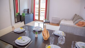 A dining area with a table set for four, a sofa, and a view of a balcony. - Appartement avec Balcon Privé  | Piscine (Les Orres)