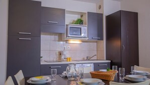 A modern kitchen with dark cabinets, a microwave, and a sink. There is a dining table set with plates, glasses, and a basket of bread. - Appartement avec Balcon Privé  | Piscine (Les Orres)