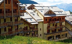 Un hôtel à plusieurs étages doté de balcons, d’un espace extérieur aménagé et couvert, et offrant une vue sur un paysage montagneux.