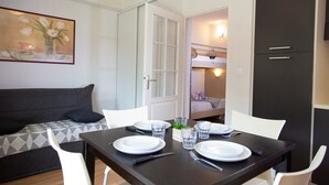 Un comedor con una mesa lista para dos personas, un sofá y una cama litera al fondo.