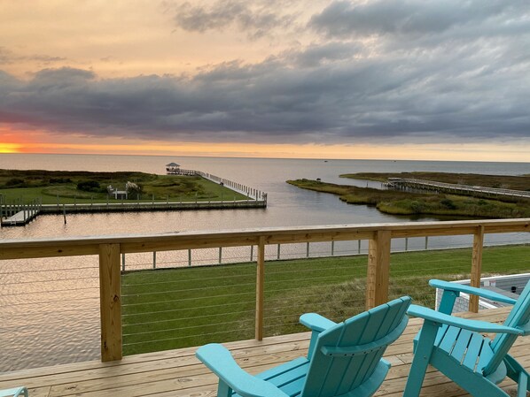 A deck with two turquoise chairs overlooking a body of water, a pier, and grassy areas.