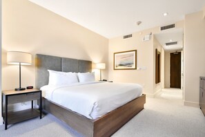 Ein ordentlich eingerichtetes Hotelzimmer mit einem großen Bett, Nachttischen mit Lampen, einem gerahmten Bild an der Wand und einer Tür zu einem anderen Raum.